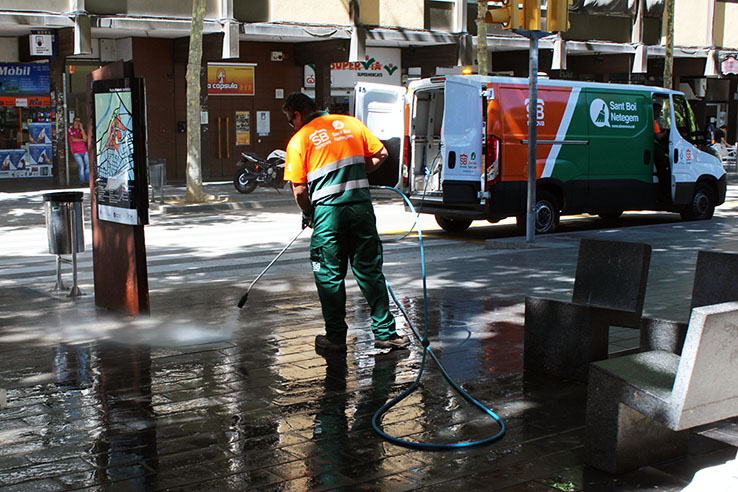 Un treballador netejant amb aigua al carrer de Torras i Bages