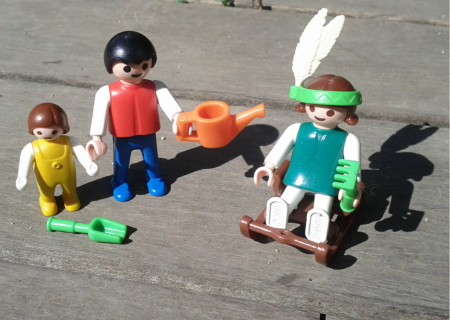 Tres ninots de playmobil sobre una estructura de fusta. Un d'ells va amb una ploma al cap com si fos un indi, l'altre porta una regadora a la mà i tercera figura petita té una pala al seu davant 