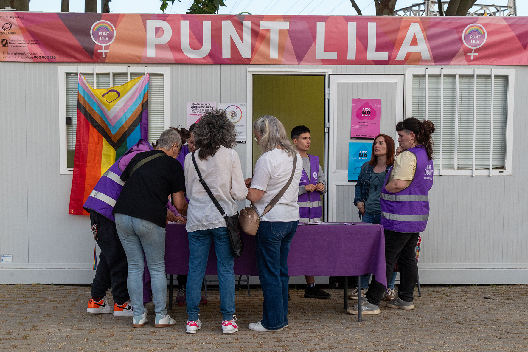Persones interessades en un punt lila on hi ha una pancarta que ho posa i també una bandera LGTBI+