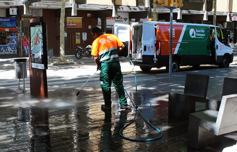 Un treballador netejant amb aigua al carrer de Torras i Bages